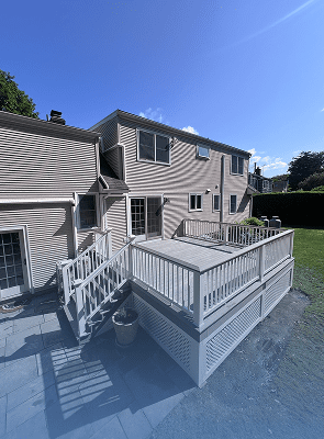 A beige two-story house with a wooden deck and white railing.