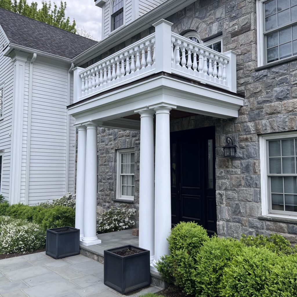 Stone house entrance with white porch and greenery.