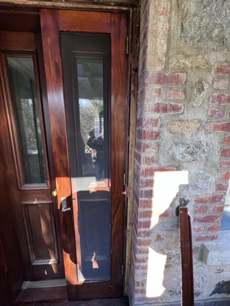A wooden door with glass panels and a brick wall beside it.