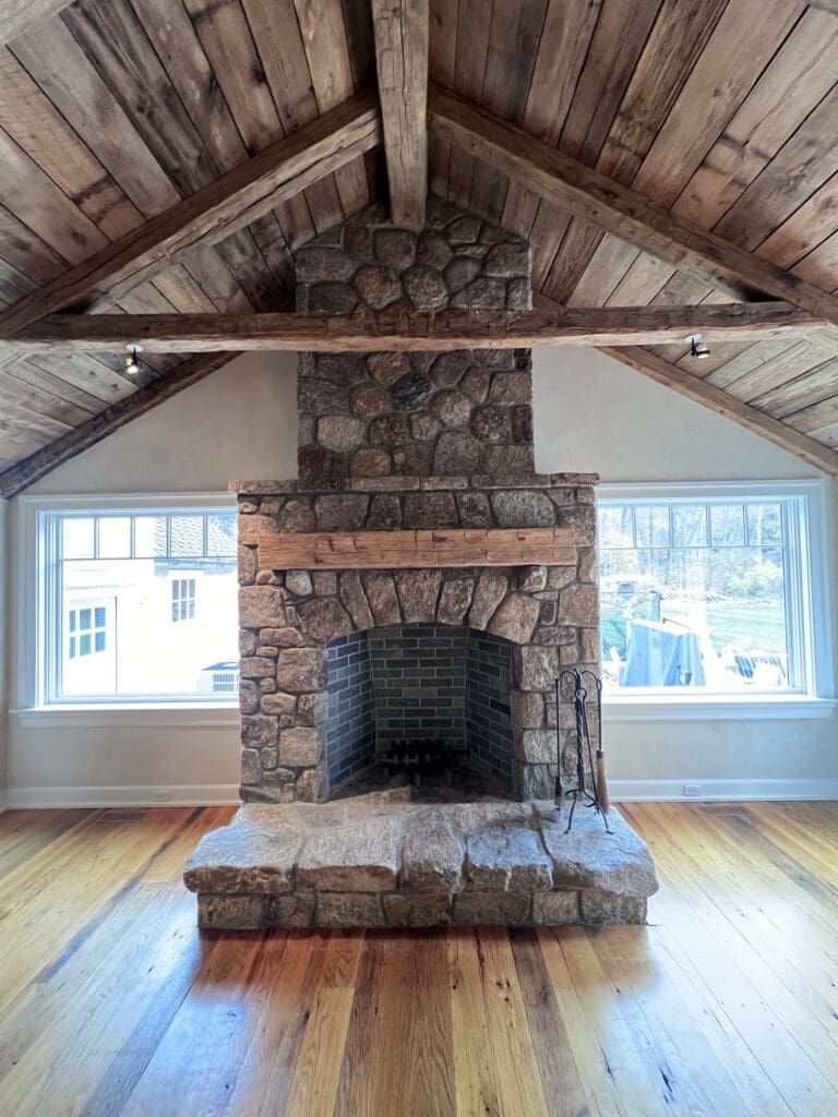 Rustic stone fireplace in a cozy wooden cabin room with large windows.