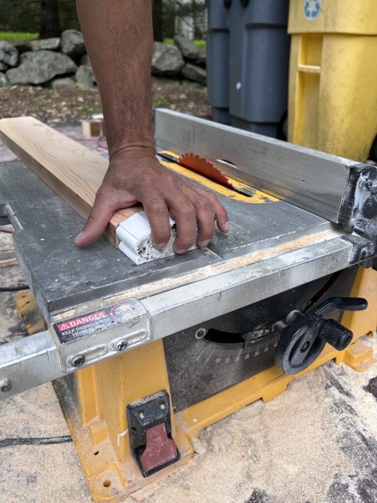 Hand adjusting a piece of wood on a table saw.