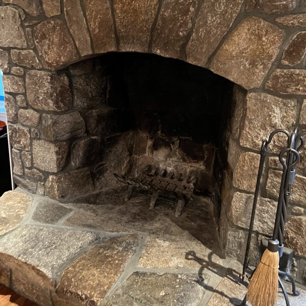 Rustic stone fireplace with a metal grate and fire tools.