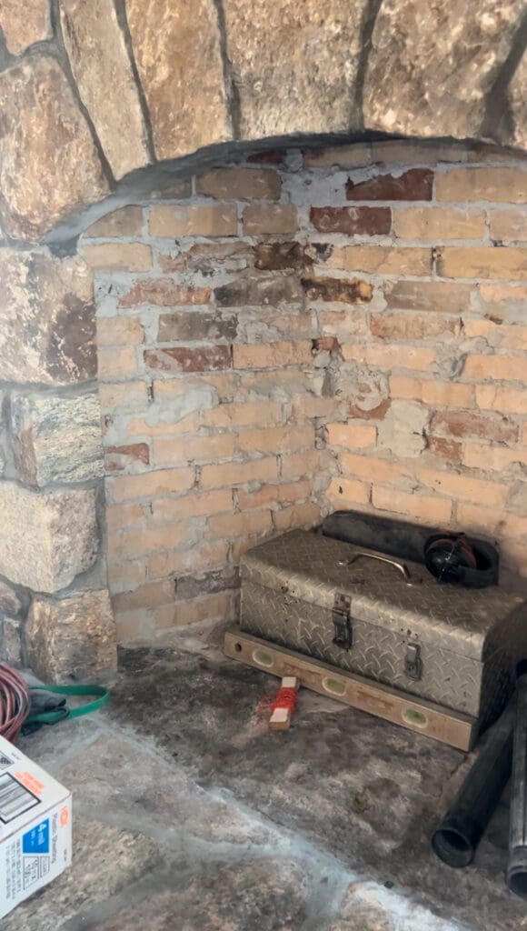 A cat resting on a metal chest in a rustic brick corner.