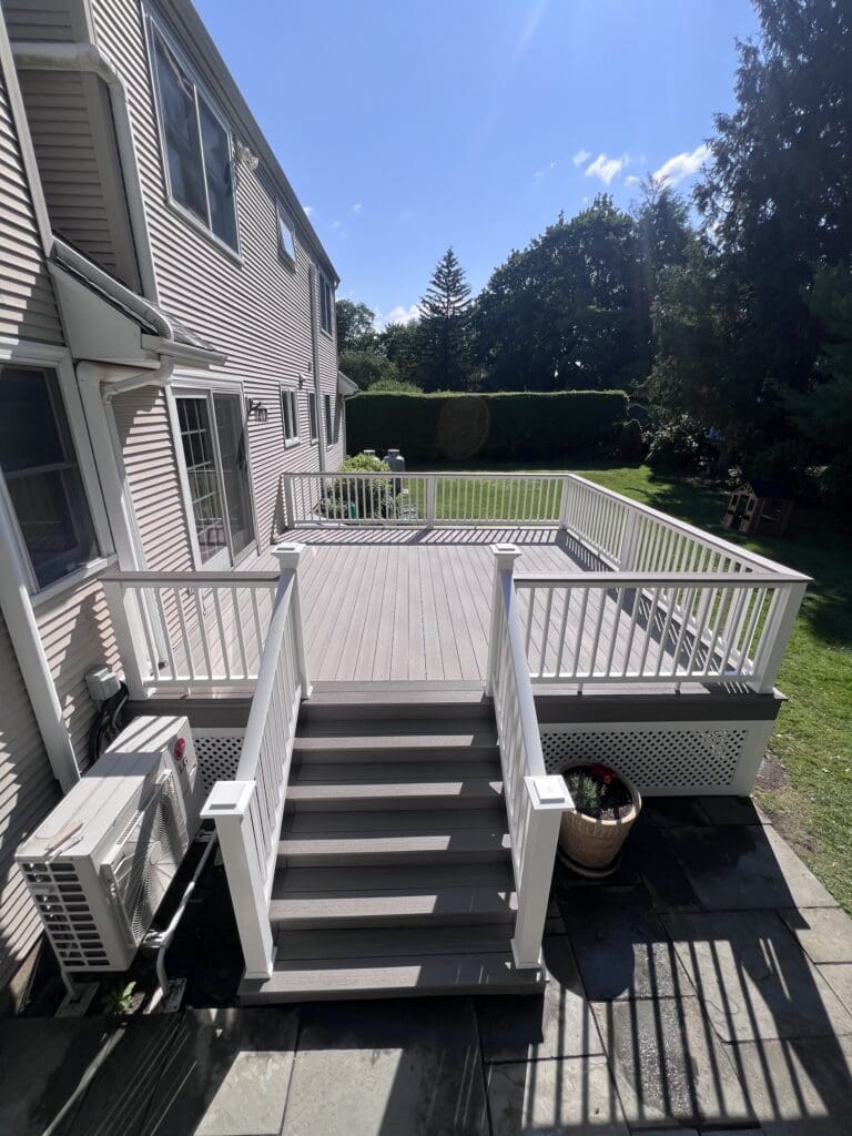 A backyard deck with white railings and a staircase leading to a grassy yard.