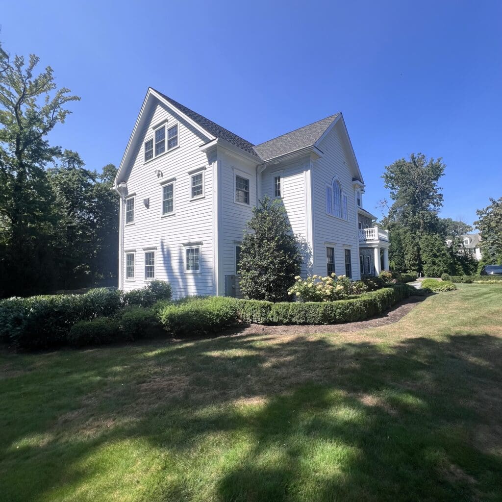 Large white colonial house with steep roof under clear blue sky.