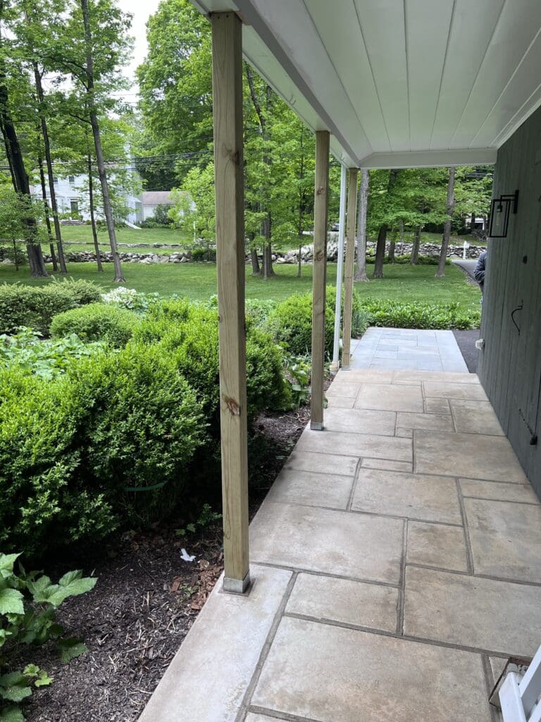 A stone-paved porch with greenery and trees around.