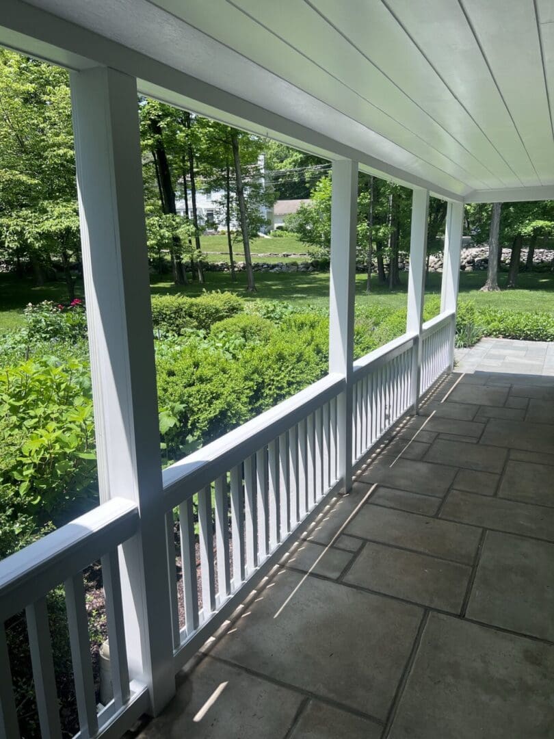 A sunlit porch with white railings overlooking a green garden.