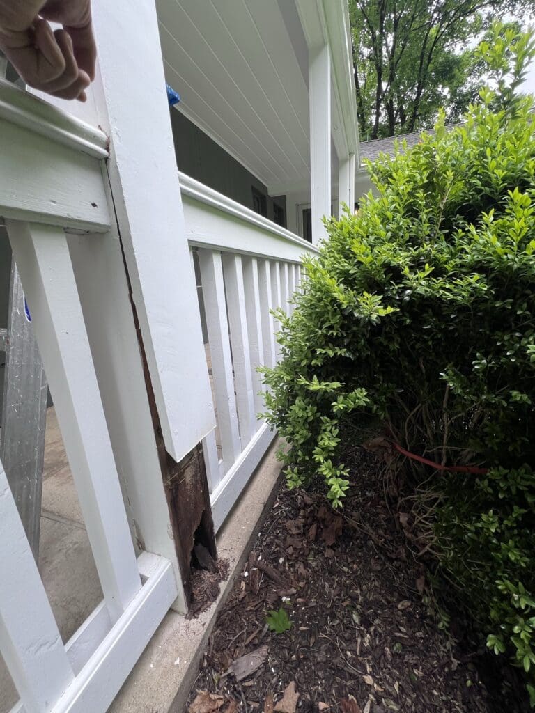 A white wooden fence with a damaged section near a green bush.