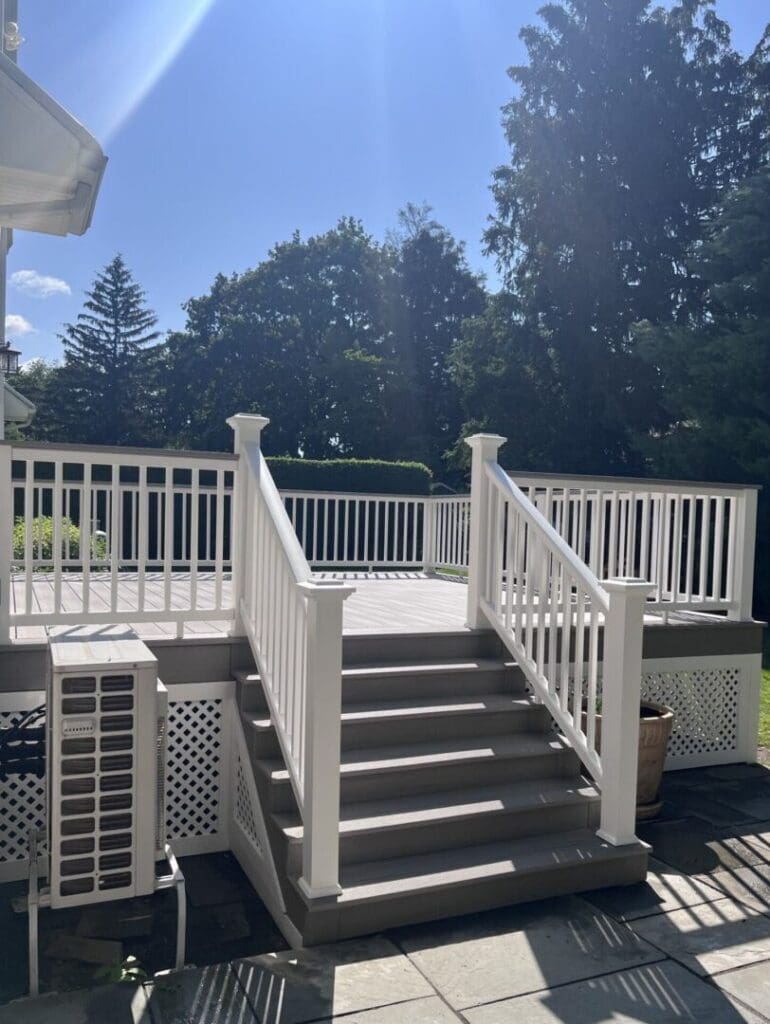 Wooden deck with stairs and white railing under a sunny sky.
