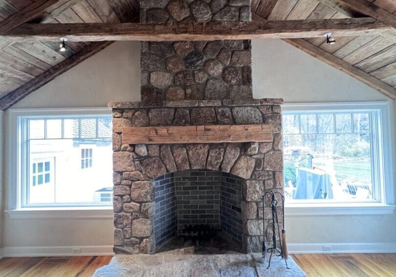 Rustic stone fireplace in a cozy wooden cabin room with large windows.