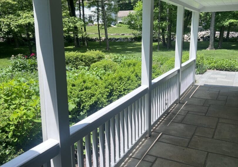 A sunlit porch with white railings overlooking a green garden.