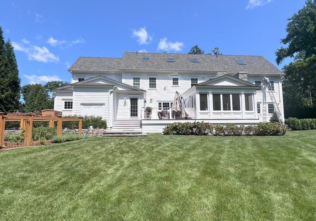 A large white house with a spacious green lawn under a clear blue sky.
